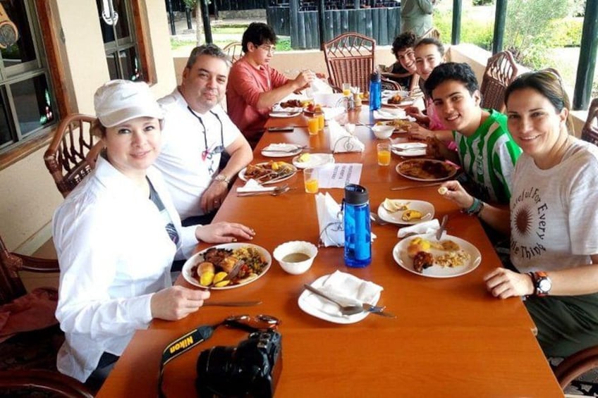 A group of people dining at a wooden table with plates of food, drinks, and a blue water bottle. 1