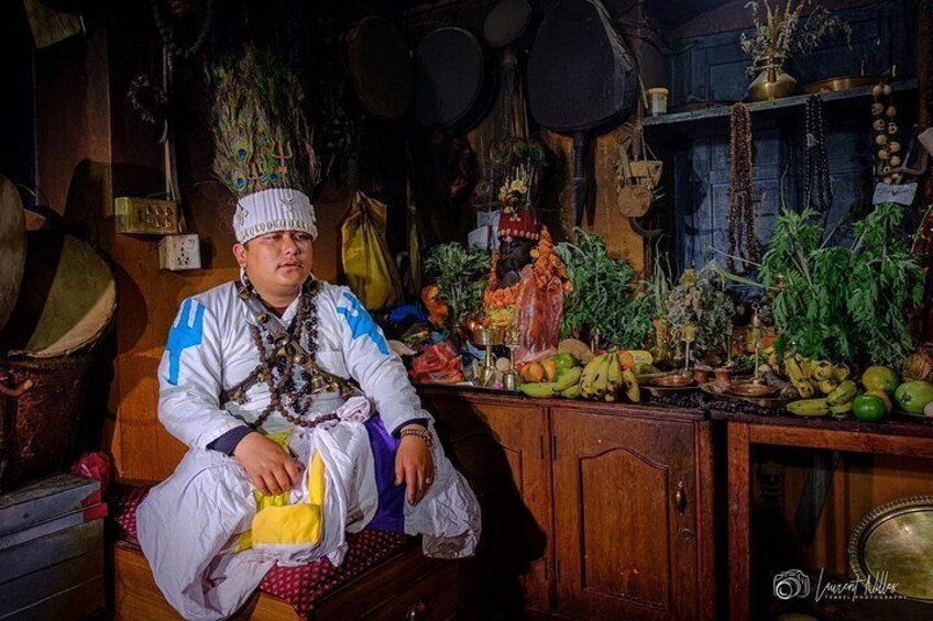 Une personne est assise sur un banc dans une pièce où se trouvent divers objets et éléments de décoration, notamment une statue, des fruits et des décorations suspendues. 4