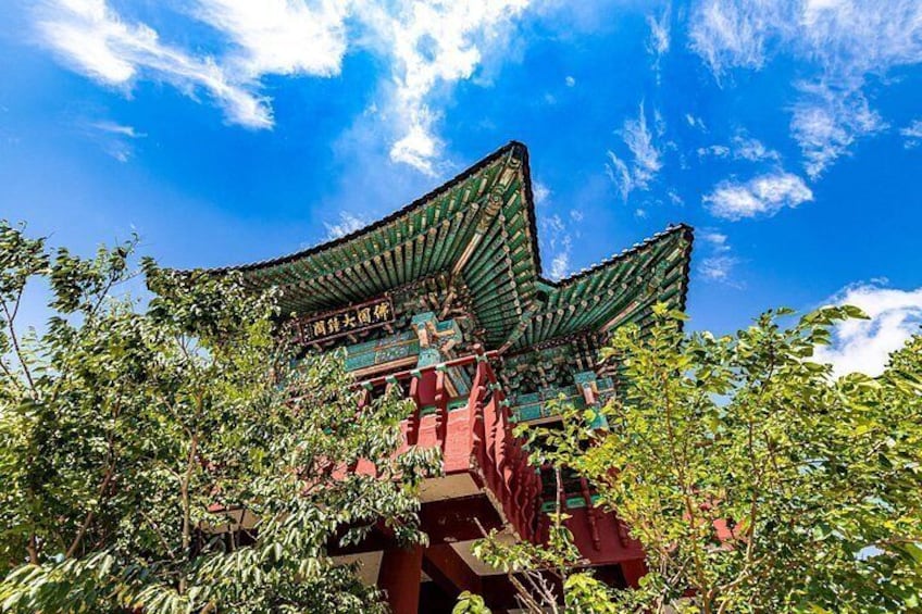 Ein traditionelles chinesisches Gebäude mit grünem Dach und roten Wänden, umgeben von üppigem Grün. 1