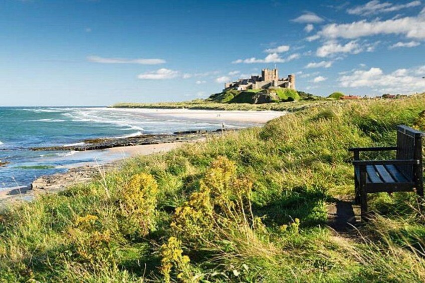 Paesaggio costiero con spiaggia, area verde e un castello su una collina. 1