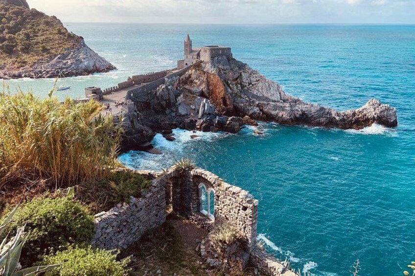 A coastal landscape with a rocky outcrop, a small tower, and a clear blue sea. 4