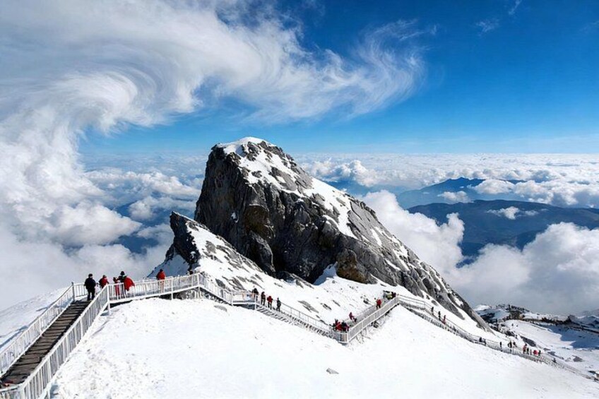A snow-covered mountain peak with a clear sky and a person standing on a viewing platform. 3