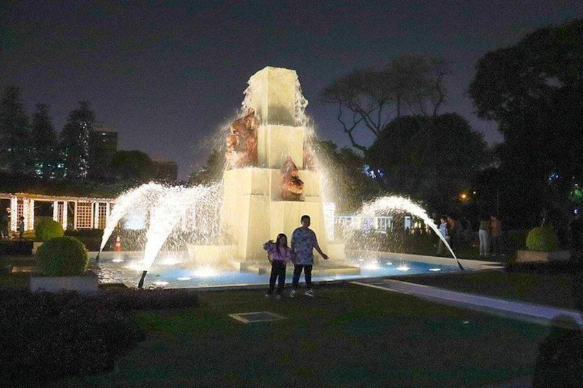 A night-time fountain with water jets, a statue, and a person standing nearby. 4