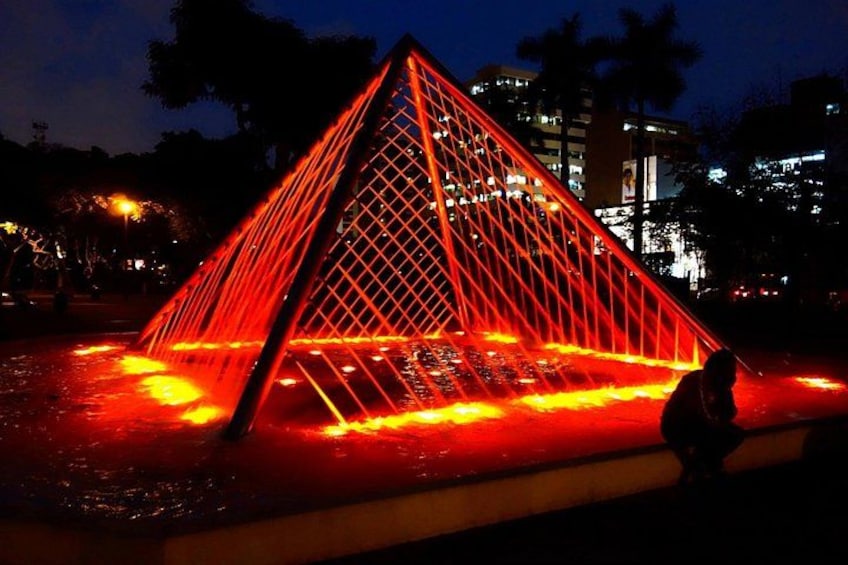 A brightly lit pyramid structure with water cascading down its sides at night. 2