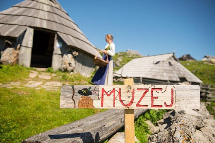A wooden sign with the word 'MUZEJ' and a drawing of a woman in traditional attire. 3