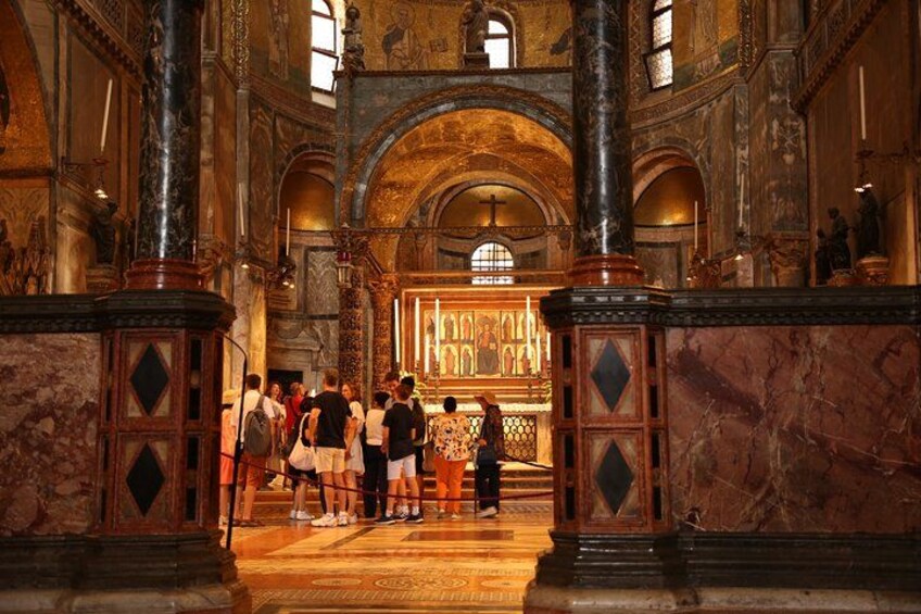 Interno di un edificio storico caratterizzato da colonne decorate, un altare centrale e un gruppo di persone radunate davanti. 3