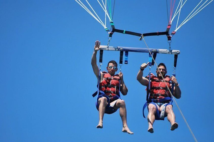 Dos personas practicando parapente, vestidas con chalecos salvavidas y arneses, con un cielo azul despejado al fondo. 3