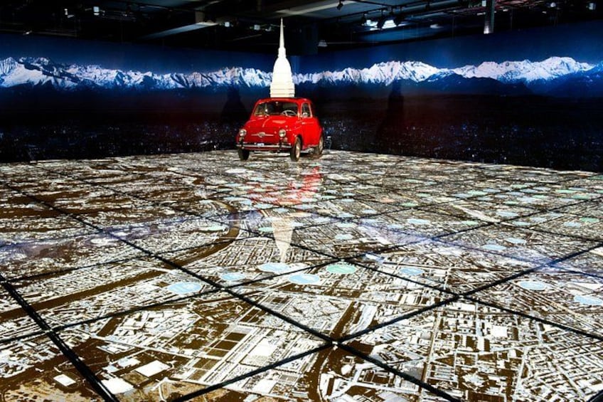 Une voiture rouge sur un sol à motifs en forme de quadrillage, avec une montagne en arrière-plan. 1