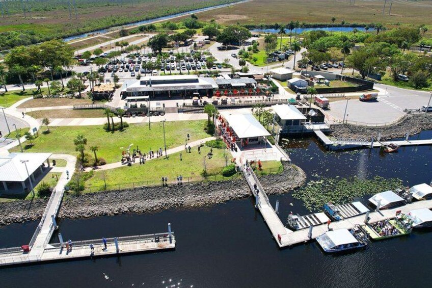 A marina with boats docked, a parking area, and a building with a flat roof. 2