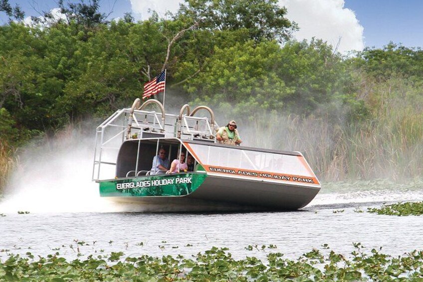 Ein Boot mit der Aufschrift 'Everglades Holiday Park' fährt durch Wasser, gesäumt von Vegetation. 1