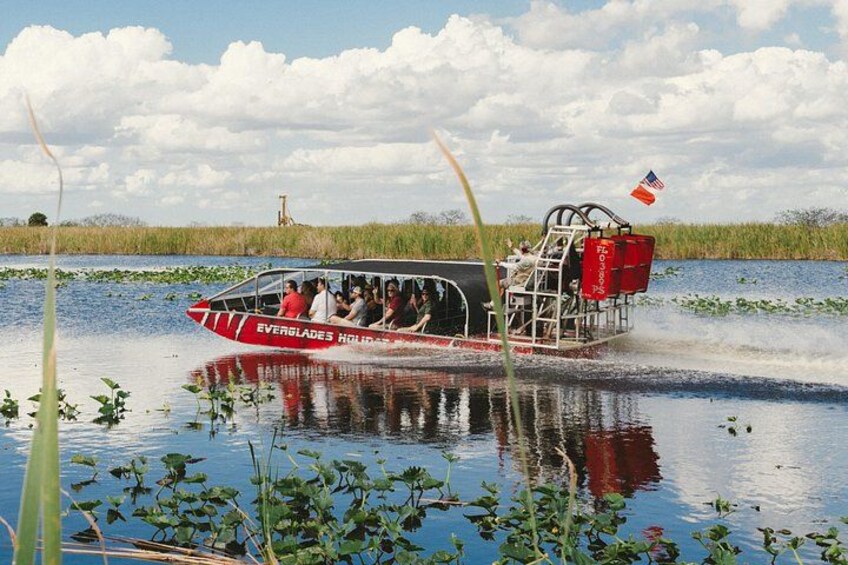 A boat with people on it, moving through water with vegetation around. 3