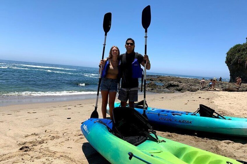 Deux personnes se tiennent sur une plage de sable, avec des kayaks et des pagaies. 1