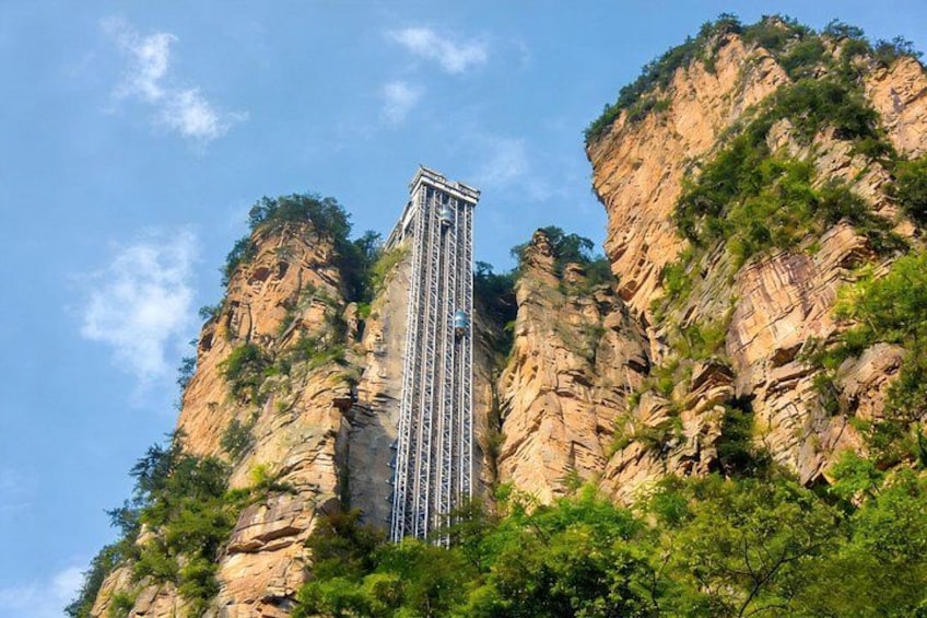 A tall structure with a metal framework, set against a backdrop of rocky cliffs and greenery. 2