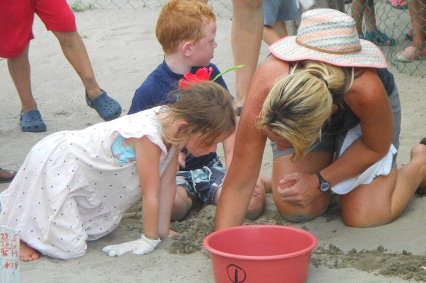 Children playing in sand, a red bucket, and adults supervising. 1