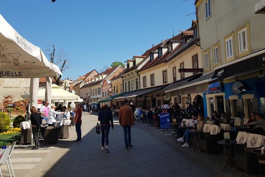 En livlig utomhusmarknad där folk promenerar och sitter, omgiven av byggnader med butiker och uteserveringar. 5