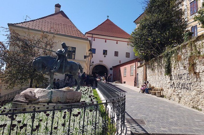 Una estatua de un hombre a caballo, un muro de piedra con grafitis y un edificio con techo rojo. 5