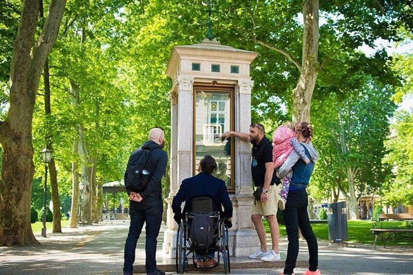 A group of people around a historical monument in a park with trees and a paved path. 2