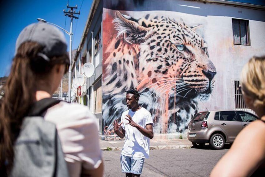 A street mural of a leopard, a man gesturing, and a car parked on the side of the road. 2