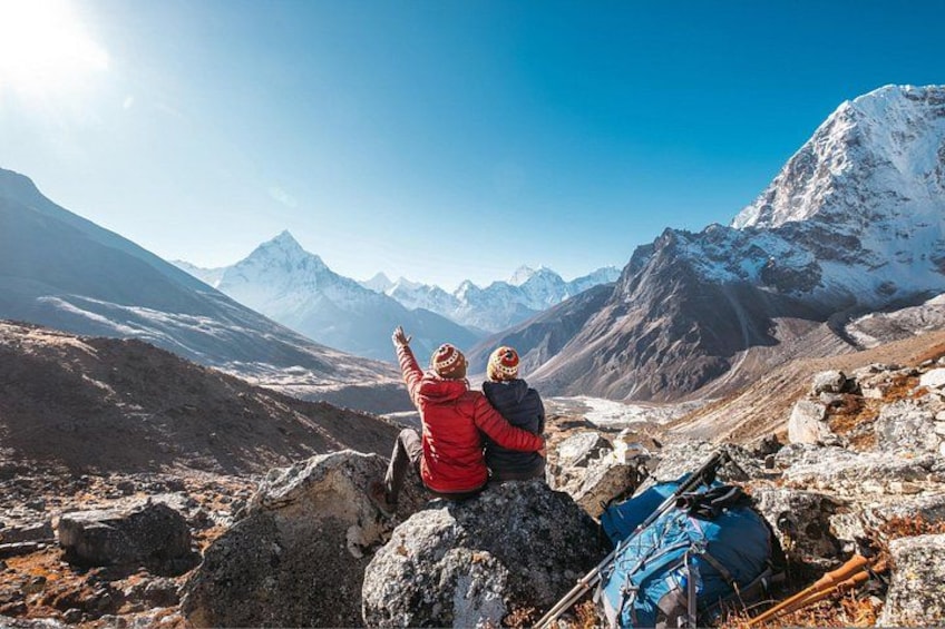 Two people sitting on a rocky outcrop, overlooking a mountainous landscape with snow-capped peaks. 4