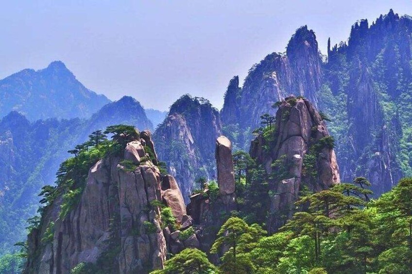 A mountainous landscape with prominent rock formations and dense green foliage. 1