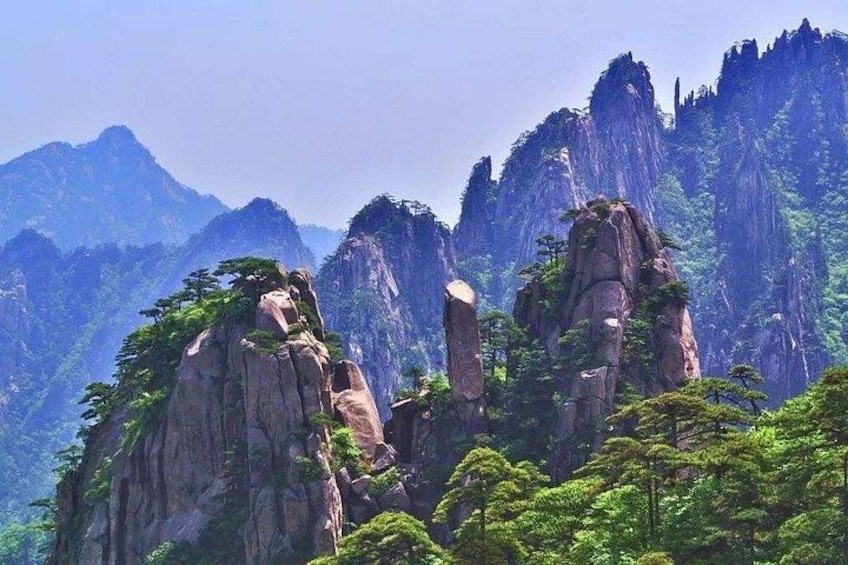 A mountainous landscape with prominent rock formations and dense green foliage. 1