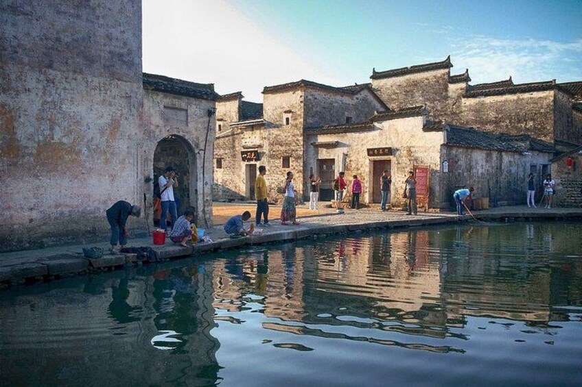 A traditional courtyard with people engaging in activities near a water body, surrounded by old buildings with distinct architectural features. 2