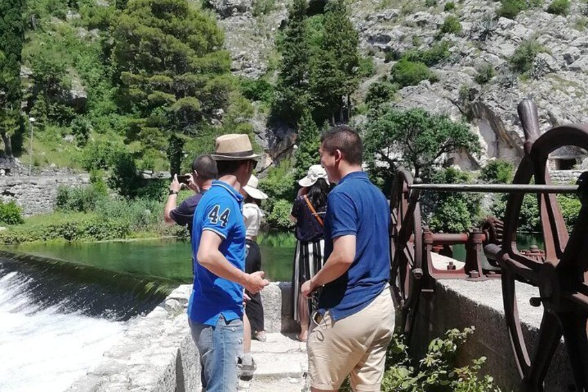 A group of people near a water mill with a river and rocky terrain in the background. 1
