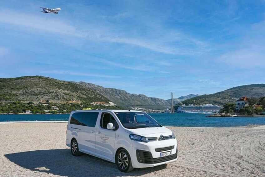A white van parked on a sandy beach with a body of water and mountains in the background. 3