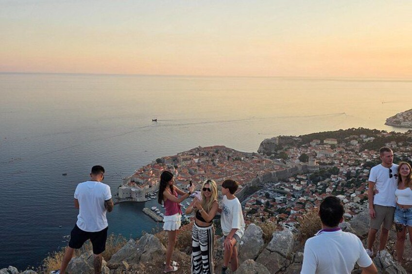 A group of people standing on a cliff overlooking a coastal town at sunset. 2