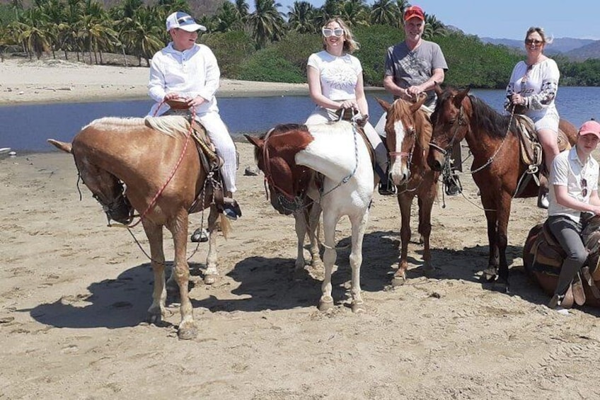 Un groupe de personnes à cheval sur une plage de sable, avec des palmiers en arrière-plan. 2
