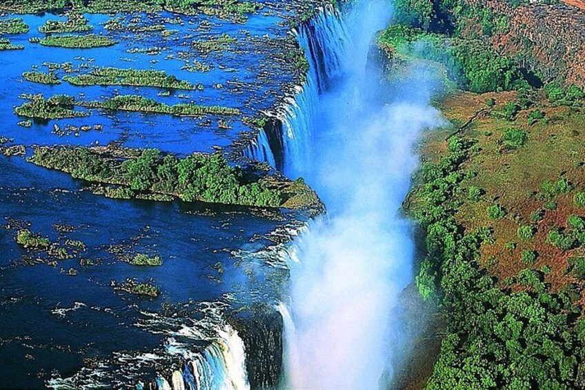 A waterfall cascading over a lush green landscape with floating vegetation. 5