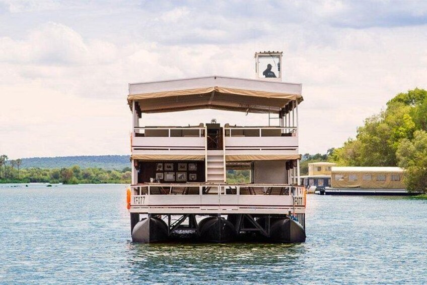 A houseboat with a covered upper deck and a lower deck, floating on a body of water. 4