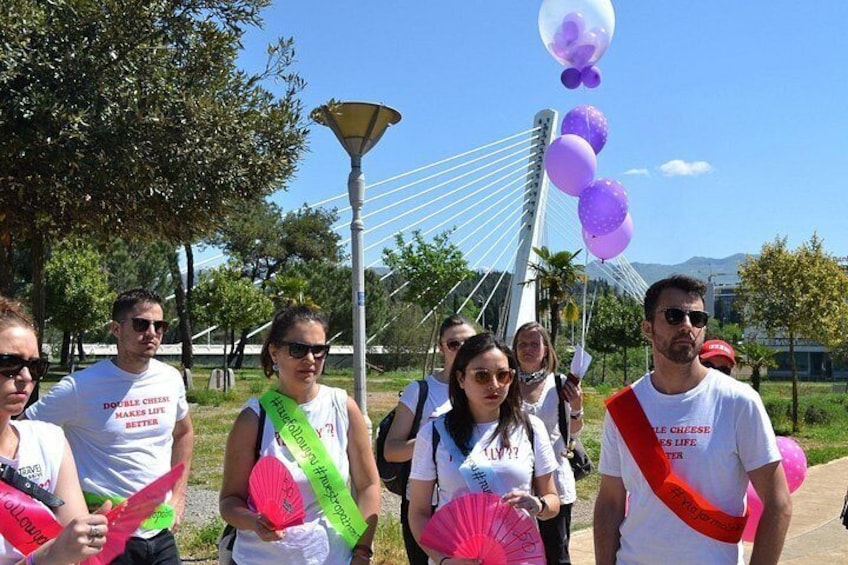 A group of people holding pink fans and balloons, standing in a park with a bridge in the background. 2