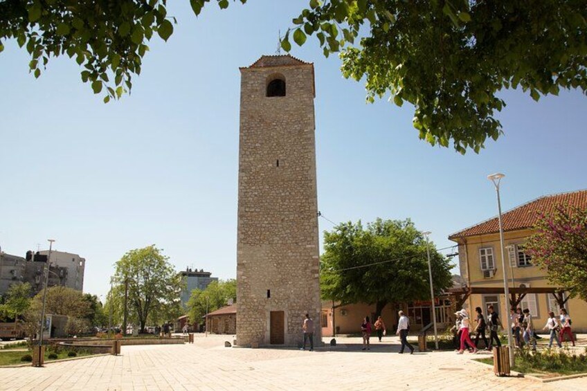 Ein Steinturm, ein gepflasterter Platz und ein gelbes Gebäude mit rotem Dach. 1