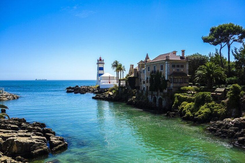 A coastal scene with a lighthouse, a large house, and clear blue waters. 2