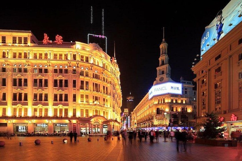 A brightly lit historic building with a clock tower, surrounded by a bustling square with people walking. 2