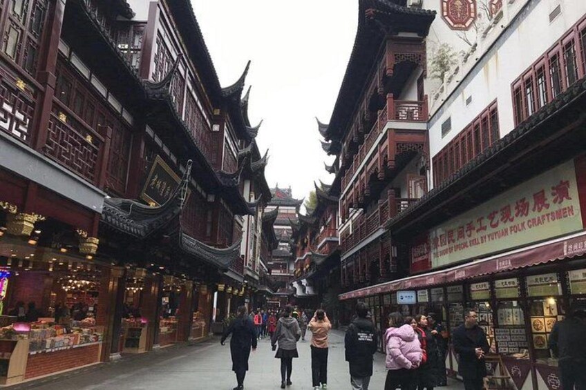 A traditional street with ornate buildings, a crowd of people, and a sign for a craft shop. 3