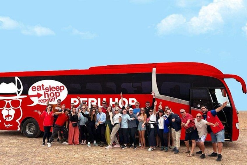 Un grupo de personas posando frente a un autobús rojo con la inscripción 'eat sleep hop repeat' y 'PERU'. 3