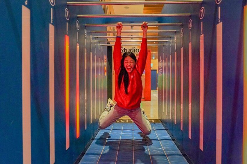A person hanging from a bar in a brightly lit hallway with vertical stripes and a sign that reads 'studio'. 5