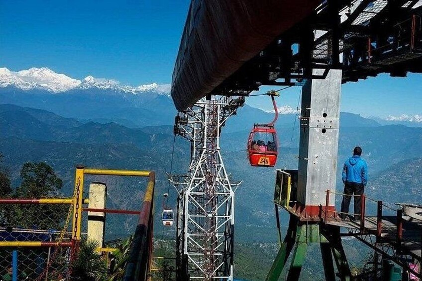 A cable car system, a person standing on a platform, and a mountainous landscape with snow-capped peaks in the background. 1