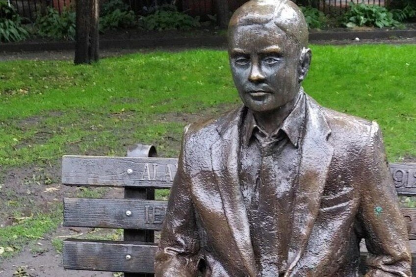 A bronze statue of a man in a suit sitting on a wooden bench. 2
