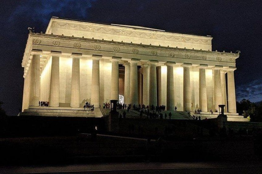 Un grand bâtiment de style néoclassique, orné de colonnes et illuminé la nuit. 1