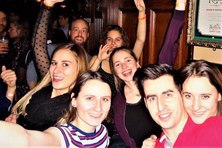 Een groep mensen in een sociale setting, mogelijk een feestje of bijeenkomst, met een houten deur en een lijst of diploma in de achtergrond. 2