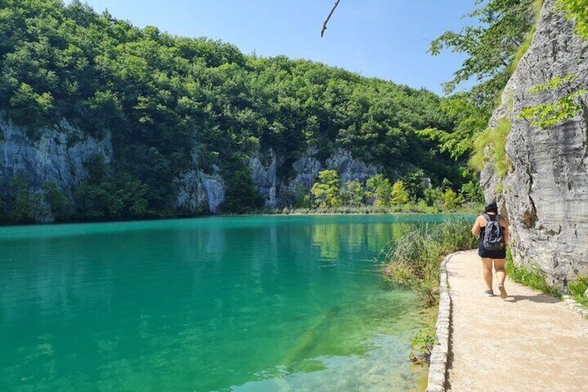 A person hiking along a path beside a turquoise lake with cliffs in the background. 3