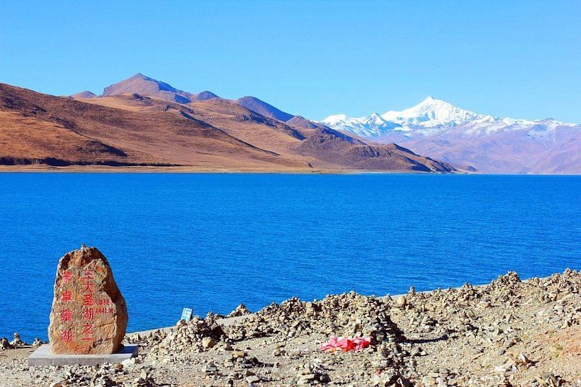 A large body of water with mountains in the background and a rock with inscriptions in the foreground. 1