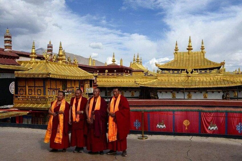 A group of monks in traditional robes standing in front of a golden temple with intricate architecture. 2