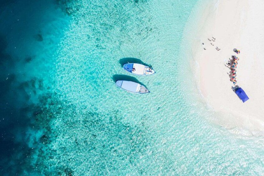 A beach with two boats anchored near the shore, a sandy beach, and a group of people. 3