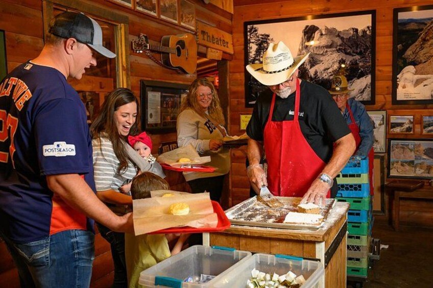 A man in a cowboy hat and red apron preparing food at a counter, with a woman and a child nearby. 2