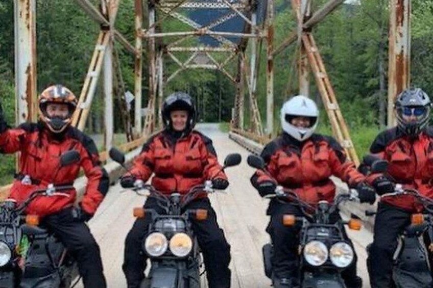 Fyra motorcyklister på en bro med en rustik metallkonstruktion. 4