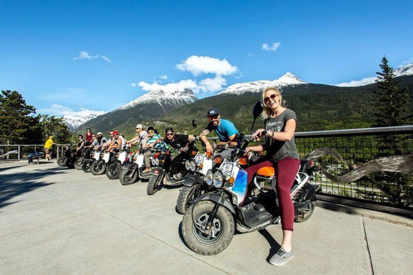 A group of people on motorcycles lined up on a bridge with a mountain in the background. 2